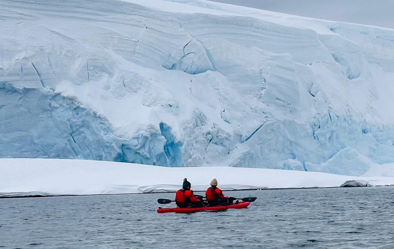 Two expedition cruise guests kayaking beside an Antarctic glacier