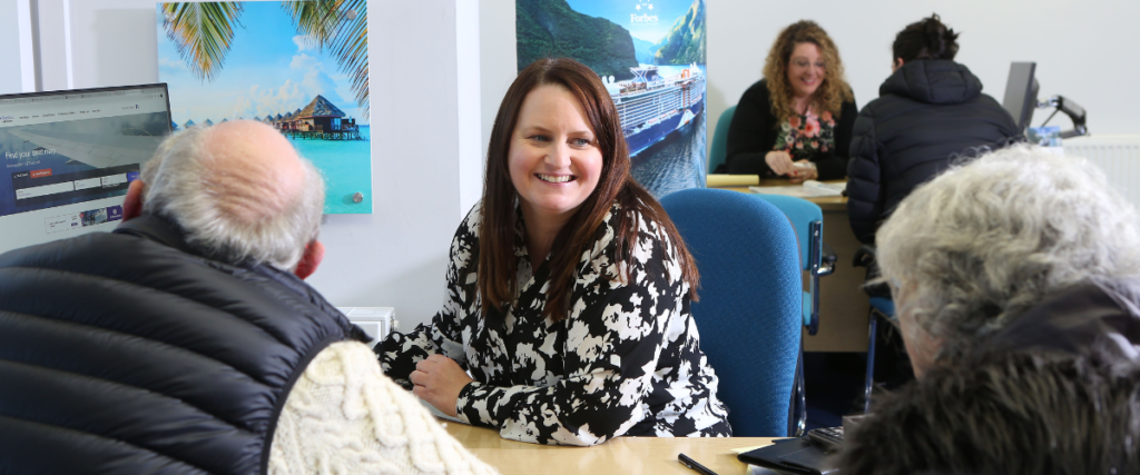 Elderly couple meeting with a female cruise consultant in an office. There is another meeting behind them.