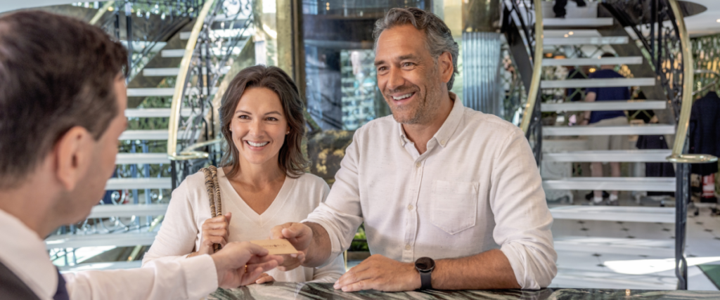 Middle aged couple checking into their cruise, being handed a room key. They are both smiling.